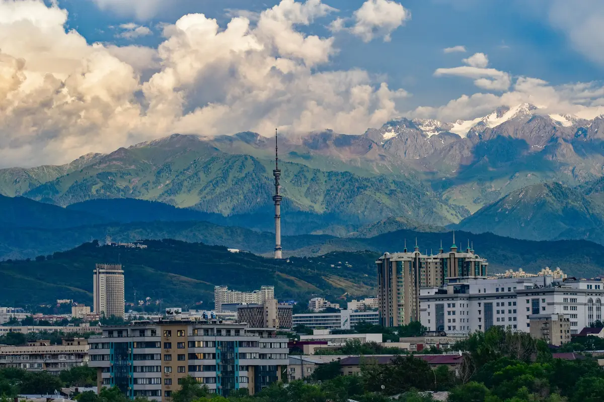 Almaty city skyline with its television tower, backed by the green slopes and snow-capped peaks of the Trans-Ili Alatau