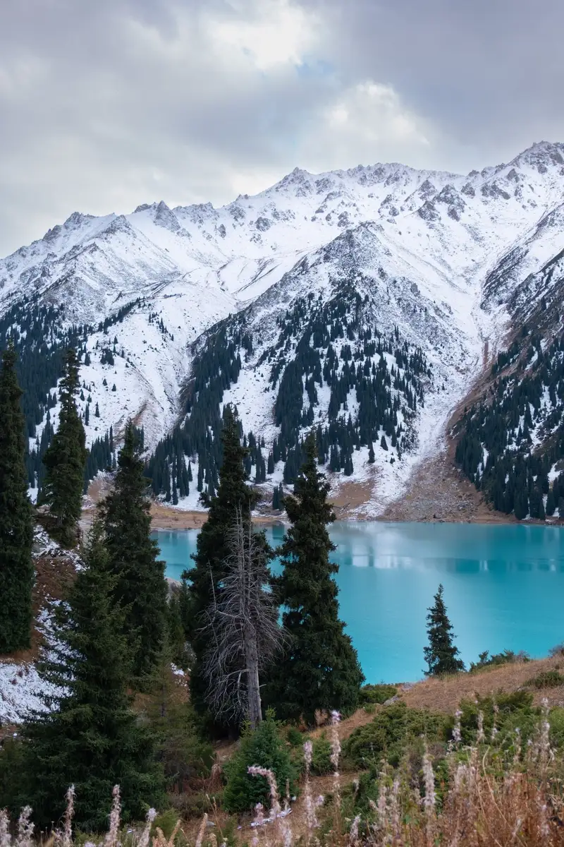 The turquoise water of Big Almaty Lake beneath snow-dusted peaks and spruce forest