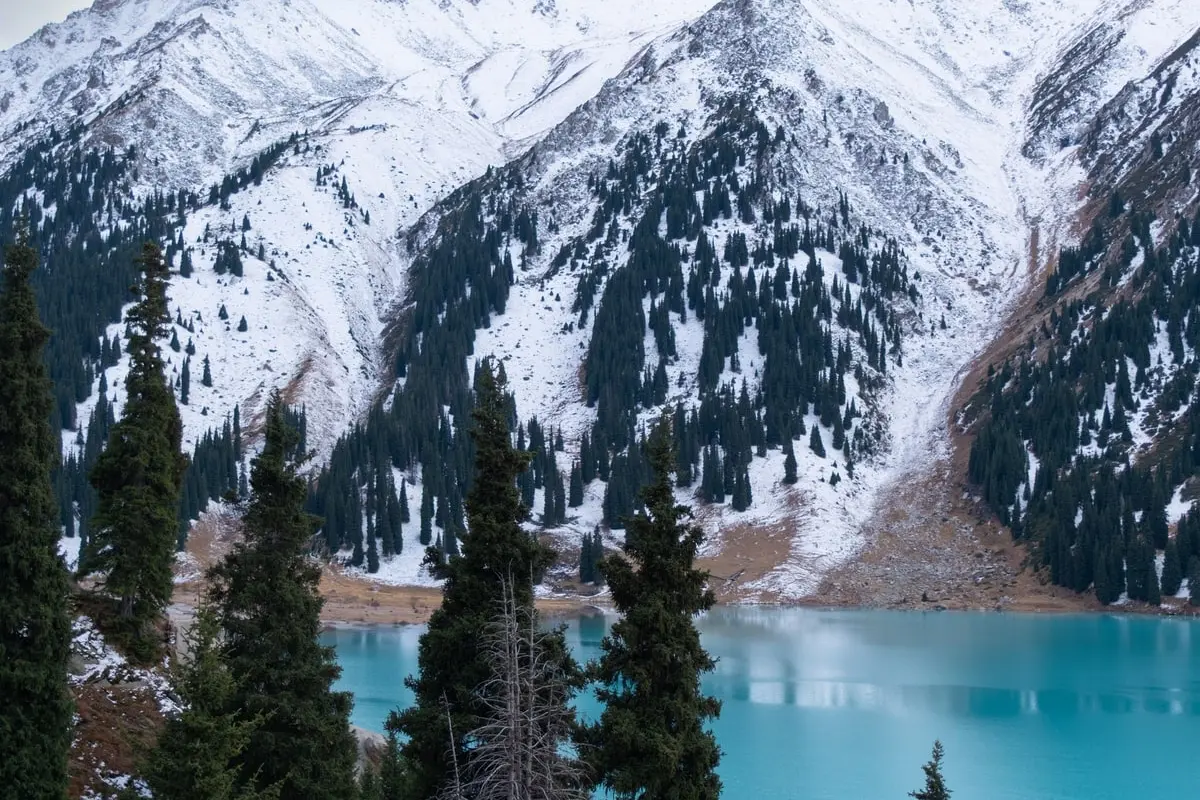 The turquoise water of Big Almaty Lake beneath snow-dusted peaks and spruce forest