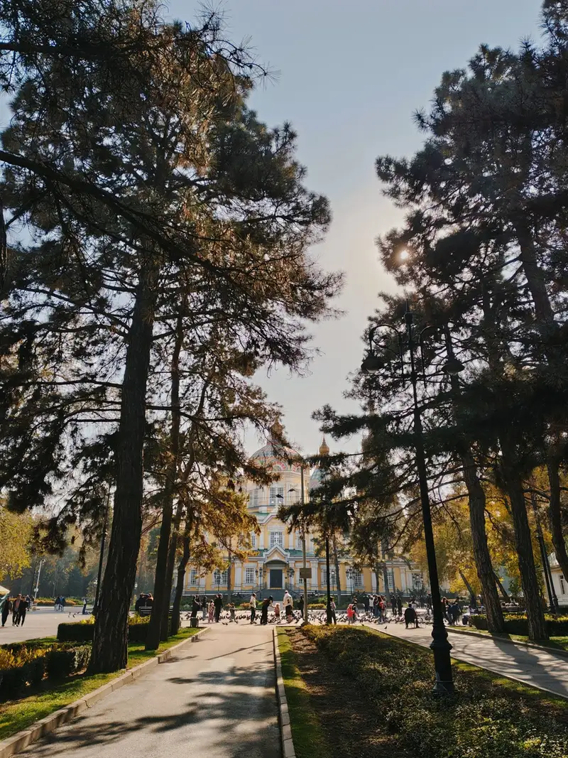 The domes of the Ascension Cathedral seen through tall pines in Panfilov Park, Almaty